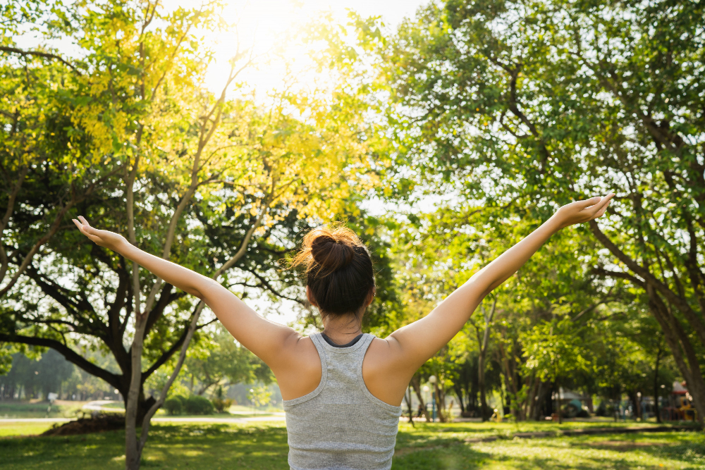 femme de dos dans un parc avec les bras ouverts