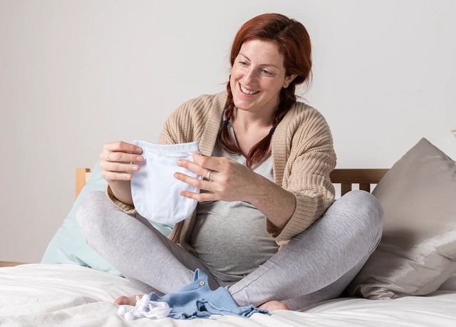 femme enceinte regardant les vêtements de bébé